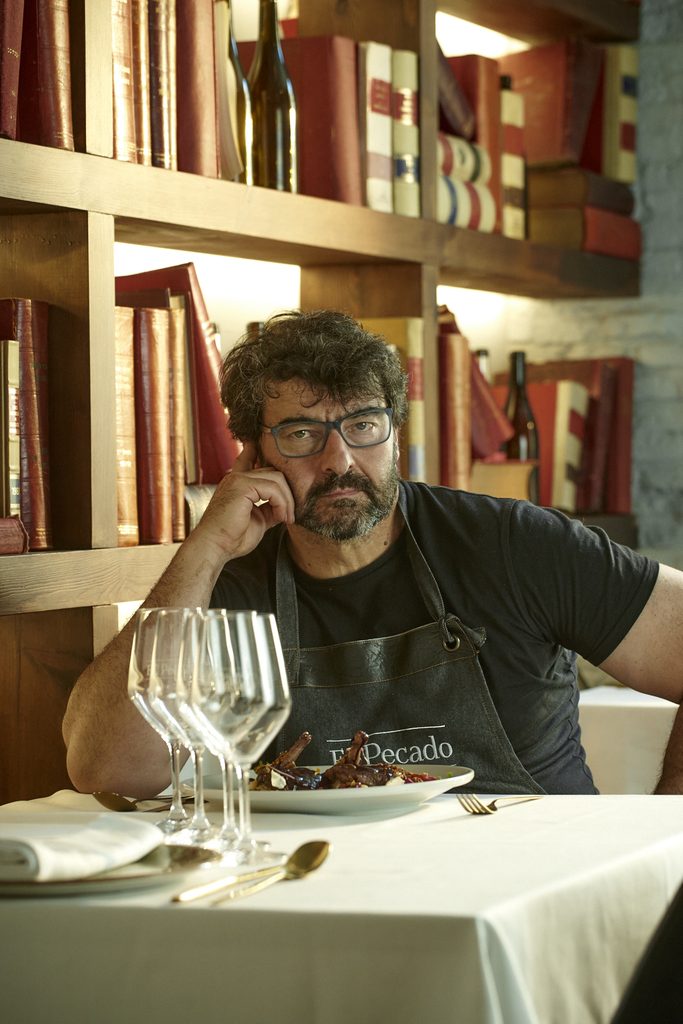 Juanma Melchor, jefe de cocina de El Pecado Restaurante Salamanca, sentado en una mesa con mantel del bonito comedor del primer piso con su emblemática librería detrás.